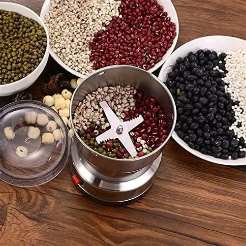 Grinding spices in a manual grinder with bowls of various seeds on a wooden surface
